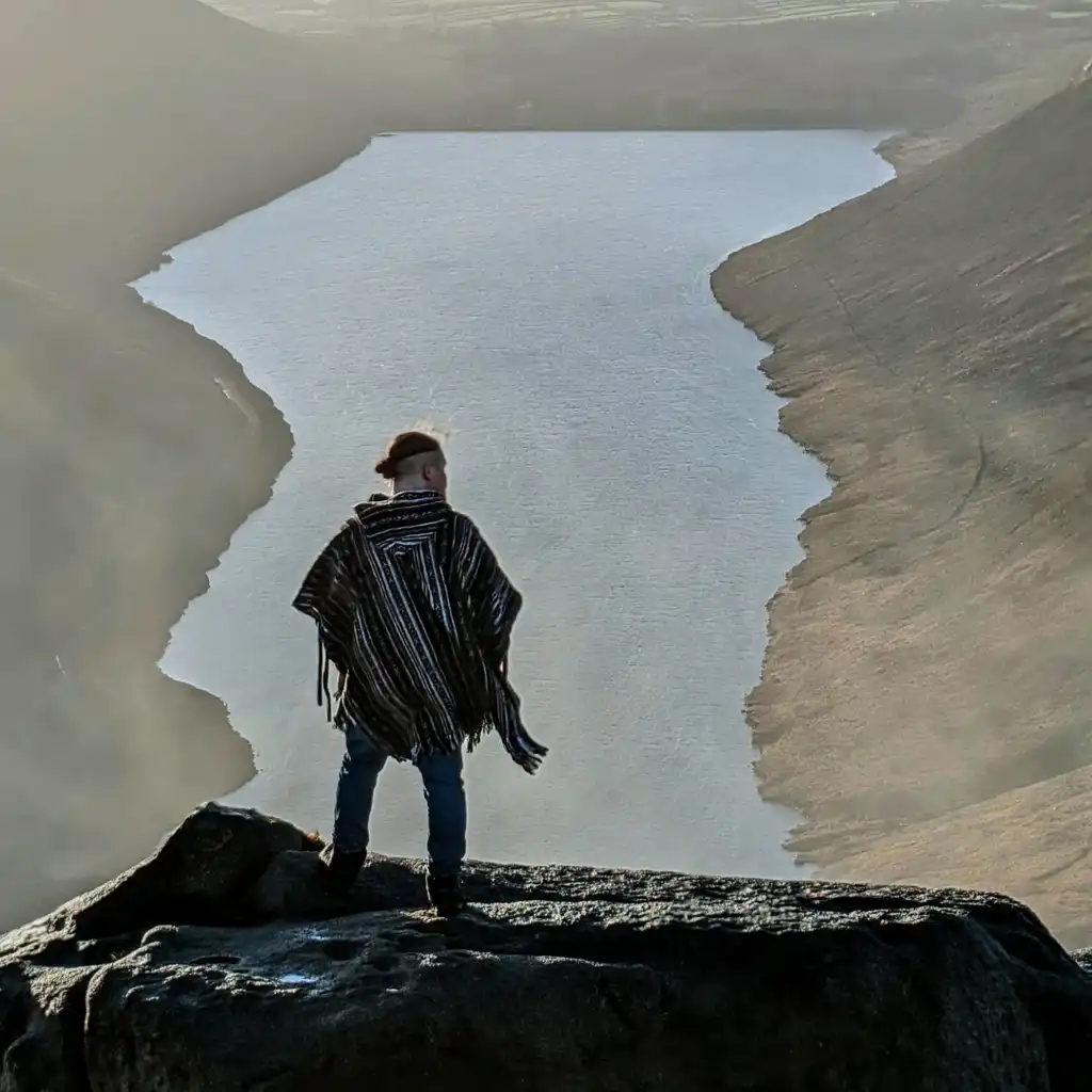 Darren Toner - a man in a poncho standing on top of a beautiful mountain overviewing a valley